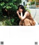 A woman sitting on a bench in front of a bush.