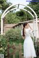 A woman in a white dress standing in front of a wooden gate.