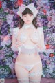 A woman in a white lingerie posing in front of a floral wall.