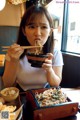 A woman eating a bowl of noodles with chopsticks.