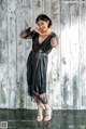 A woman in a black dress posing in front of a wooden wall.