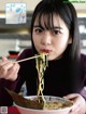 A woman eating a bowl of noodles with chopsticks.