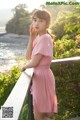 A woman in a pink dress standing on a wooden railing.