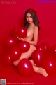 A naked woman sitting on a pile of red balloons.