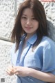 A woman in a blue shirt leaning against a wall.