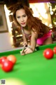 A woman in a bikini playing pool on a green table.