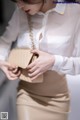 A woman in a white shirt and beige skirt holding a beige purse.