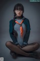 A woman in a blue jacket and orange tie sitting on the ground.