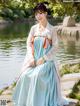 A woman in a blue and white dress sitting by a pond.